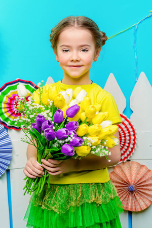 Portrait of a cute smiling girl with a bouquet of tulips in summer decorations. Kid's fashion. Summer style.の写真素材