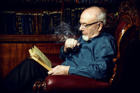 An old intelligent man reading a book in his library at home. Retirement. Retro style.の写真素材