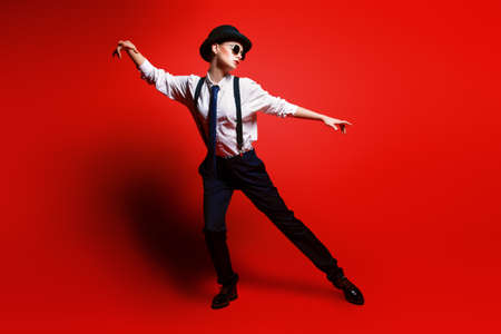Fashion shot. Attractive young model posing in a man's suit and bowler hat. Man's style clothing. Red background.の写真素材
