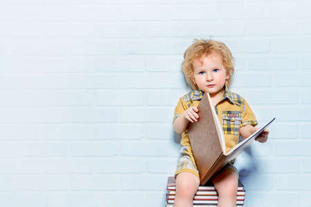 Cute little boy sitting on a stack of books with opened book. Educational concept.の写真素材