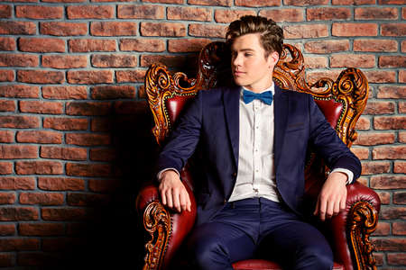 Portrait of a stylish handsome young man sitting in vintage armchair. Fashion shot. Men's clothing and accessories.の写真素材