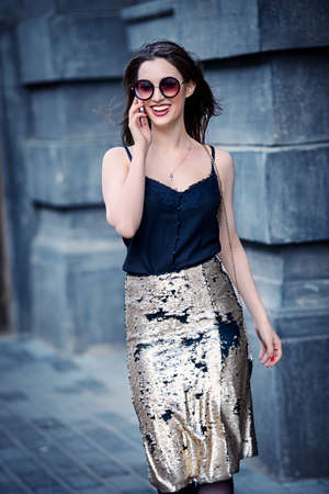 Beautiful brunette woman talking on her cell phone walking down the city street. Beauty, fashion outdoor.の写真素材