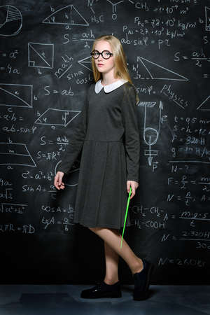 Education. Smart student girl wearing black school dress standing by a blackboard. Chalkboard background.の写真素材