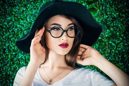 Beautiful summer girl standing by a boxwood fence. Beauty, makeup and cosmetics. Summer holidays.の写真素材
