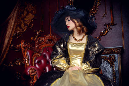 Portrait of a beautiful young woman in the lush expensive dress and elegant broad-brimmed hat in an old palace interior. Vintage style. Fashion. Renaissance Style.の写真素材