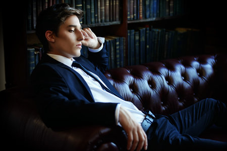 Handsome well-dressed young man by the bookshelves in a room with classic interior. Business style.