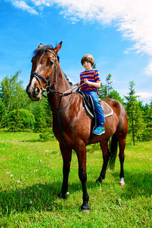 The boy is riding a horse in the park. Sunny summer day.の写真素材