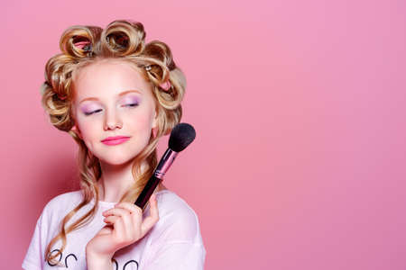 Portrait of a pretty girl teenager with curlers in her blonde hair and brushes. Teen style, fashionable teen girl. Cosmetics and make-up.の写真素材