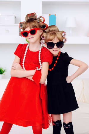 Two funny little girls with curlers in their hair are preparing for a party. Kid's fashion. Family at home.の写真素材