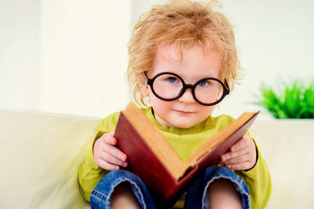 Small three year old boy in glasses is reading fairy tales. Educational concept.の写真素材