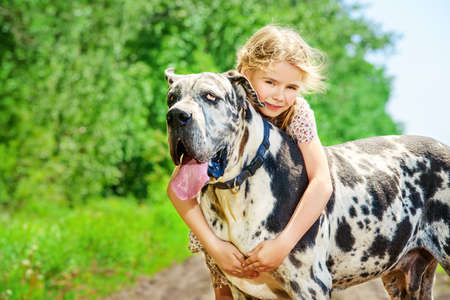 Happy little girl embracing her dog mastiff. Sunny summer day in the countryside.の写真素材