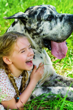 Happy little girl embracing her dog mastiff. Sunny summer day in the countryside.の写真素材