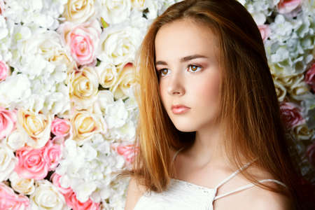Beautiful romantic young woman with nude makeup posing on a background of roses. Perfume, cosmetics concept.の写真素材