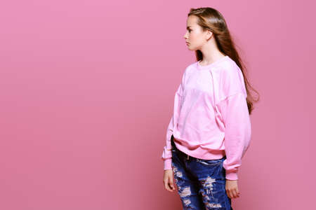 Teen style. Beautiful young model with long hair posing at studio in jeans and pink sweatshirt. Beauty, fashion.の写真素材