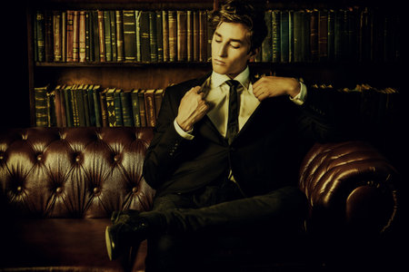 Handsome well-dressed young man by the bookshelves in a room with classic interior. Business style.の写真素材
