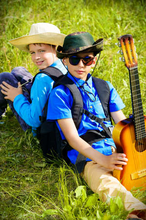 Two boys friends go hiking with a guitar and a backpacks. Sunny summer holidays. Outdoor activities.の写真素材