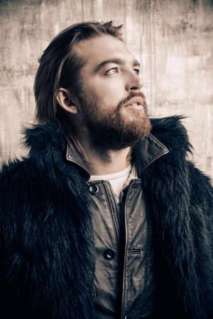 Fashion shot of a stylish brutal bearded man wearing fur coat. Studio shot over grunge background.の写真素材