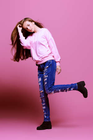 Teen style. Beautiful young model with long hair posing at studio in jeans and pink sweatshirt. Beauty, fashion.の写真素材