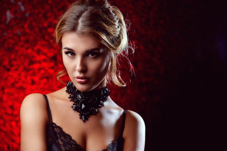 Charming young woman with evening make-up and hairstyle over red background. Jewellery, earrings and...