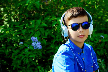 Portrait of a cool boy listening to music with headphones in a summer park. Sunny day.の写真素材
