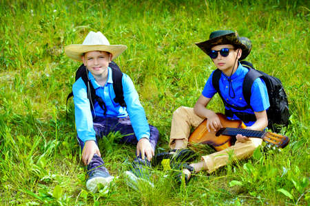 Two boys friends go hiking with a guitar and a backpacks. Sunny summer holidays. Outdoor activities.の写真素材