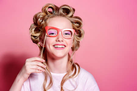 Portrait of a pretty girl teenager with curlers in her blonde hair making faces with mask. Teen style, fashionable teen girl. Cosmetics and make-up.の写真素材