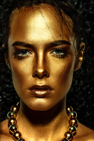 Beauty concept. Close-up portrait of a beautiful young woman with glowing golden skin. Skin care products, cosmetics. Jewellery concept.の写真素材