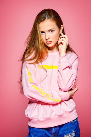 Teen style. Beautiful young model with long hair posing at studio in jeans and pink sweatshirt. Beauty, fashion. の写真素材