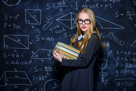 Education. Smart student girl wearing black school dress standing by a blackboard. Chalkboard background.の写真素材