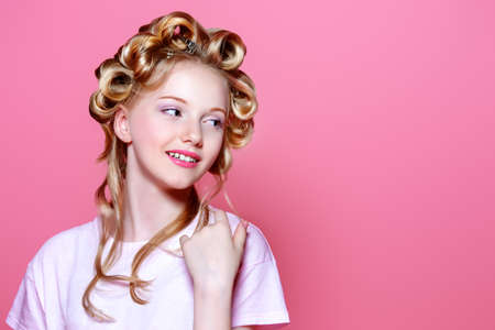 Portrait of a pretty girl teenager with curlers in her blonde hair. Teen style, fashionable teen girl. Studio shot over pink background.の写真素材
