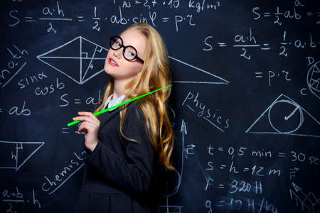 Education. Smart student girl wearing black school dress standing by a blackboard. Chalkboard background.の写真素材