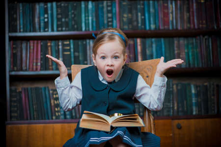 Funny excited girl sitting with opened book in a library. Educational concept.の写真素材