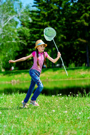 Cheerful girl with a butterfly net runs around the lawn on a sunny summer day.の写真素材