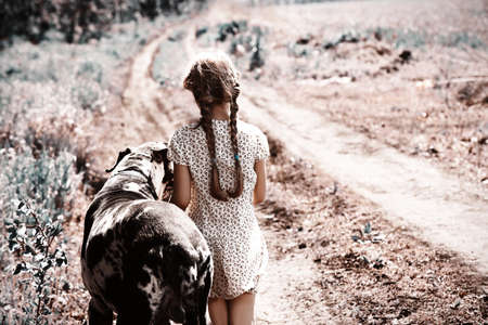 Cute girl with her dog walking along a rural road.の写真素材