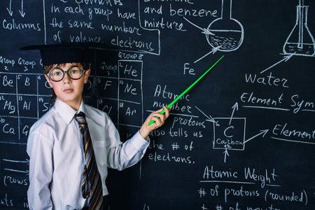Smart schoolboy answering by a blackboard on a chemistry lesson. Educational concept.の写真素材
