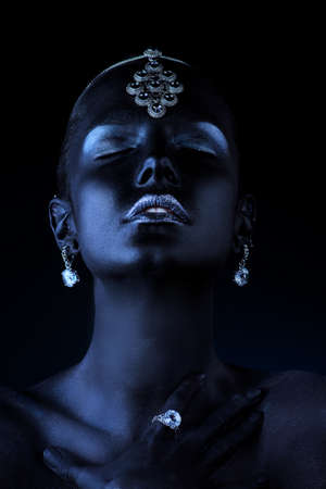 Beauty, fashion portrait. Close-up portrait of a beautiful young woman with black skin, silver glitter lips and beautiful jewelry. Body painting project. Make-up and jewelry.の写真素材