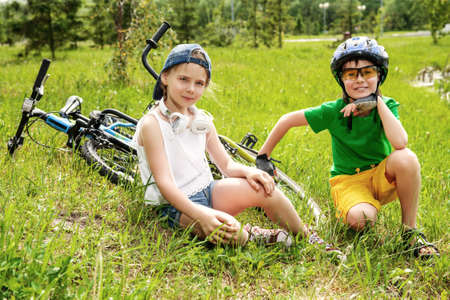 Two happy children are resting on a green lawn after riding their bikes. Happy summer holidays.の写真素材