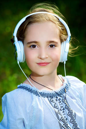 Portrait of a cute girl with headphones in a summer park. Sunny day.の写真素材