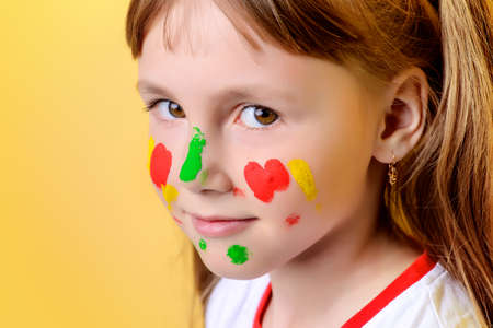 Funny little girl with paints on her face. Drawing. Yellow background.の写真素材