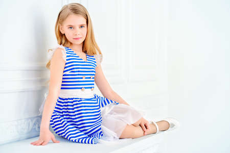 Cute little girl in a beautiful summer dress posing in a room with classical white interior. Kid's fashion.の写真素材