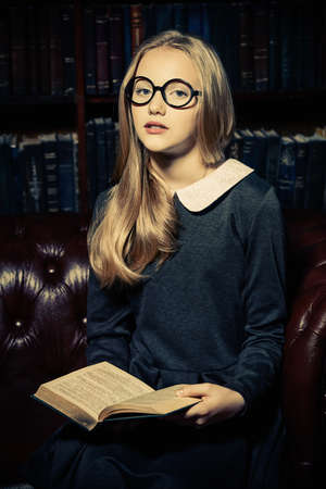 Smart student girl wearing black school dress and glasses is studying at the old library. Fairy vintage style. Education.の写真素材