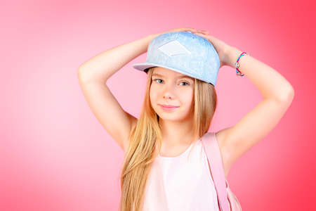 Children's fashion. Cute eight year old girl wearing summer jeans clothes and a bag posing over pink background. Studio shot.の写真素材