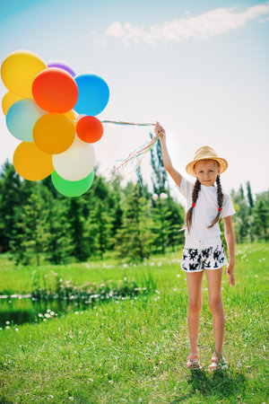 Portrait of a happy girl with many colorful balloons in the park. Summer holidays. Birthday.の写真素材