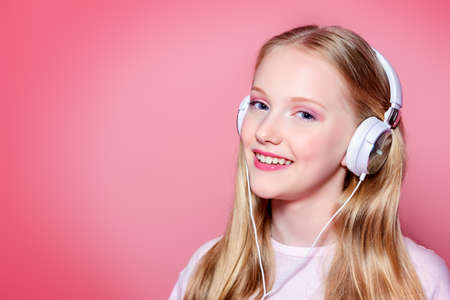 Portrait of a cute modern girl teenager with headphones over pink background. Studio shot. Teen's fashion.の写真素材