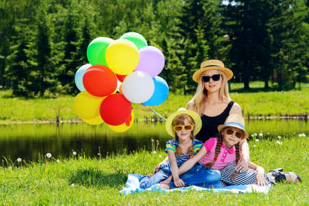 Happy summer day. Cheerful girls resting with their beloved mother in the park. Family concept.の写真素材