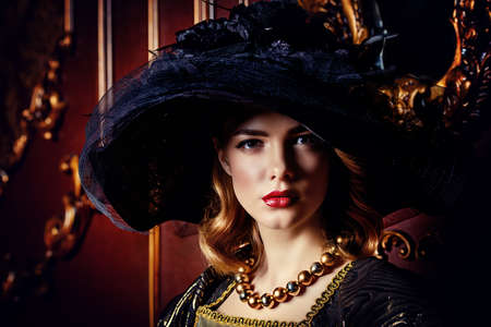 Portrait of a beautiful young woman in the lush expensive dress and elegant broad-brimmed hat in an old palace interior. Vintage style. Fashion. Renaissance Style.の写真素材