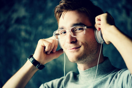 Handsome young man listenig to music in headphones and smiling.