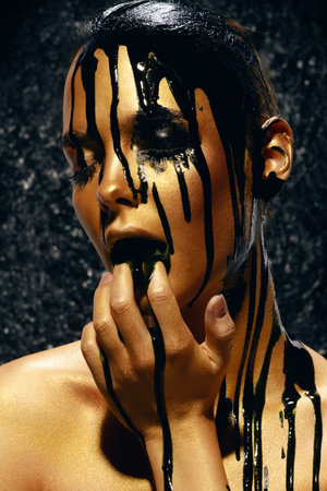 Beauty provocation. Body painting project. Portrait of a young woman with golden skin and black oil...
