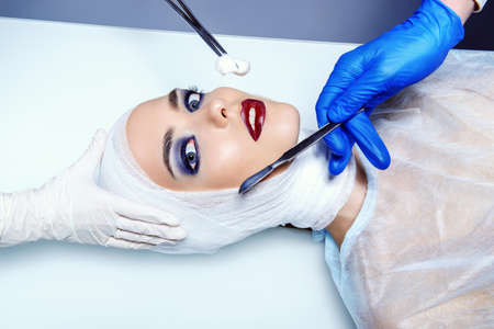 Beauty, fashion and medicine, plastic surgery. Portrait of an attractive young woman in bandages and hospital gown lying on the operating table.の写真素材