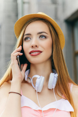 Happy girl enjoys her life, walks around the city in headphones and with a smartphone. Beauty,...